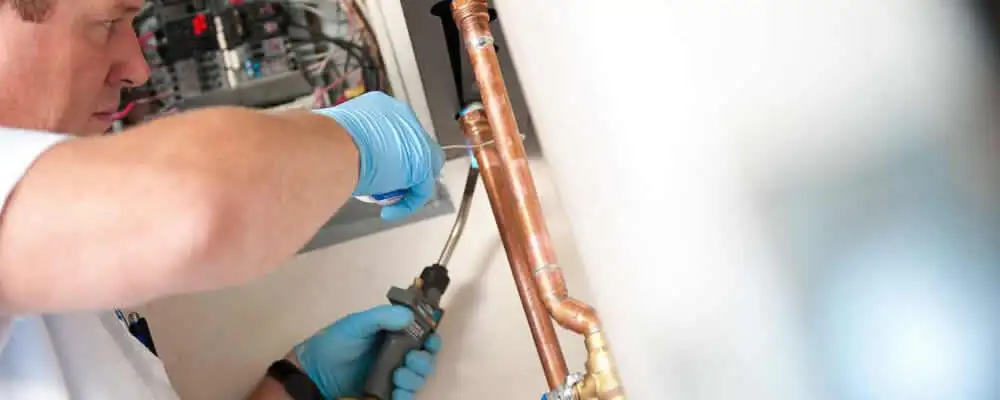 Water heater repair technician testing copper pipe connections and controls in Kansas City, KS